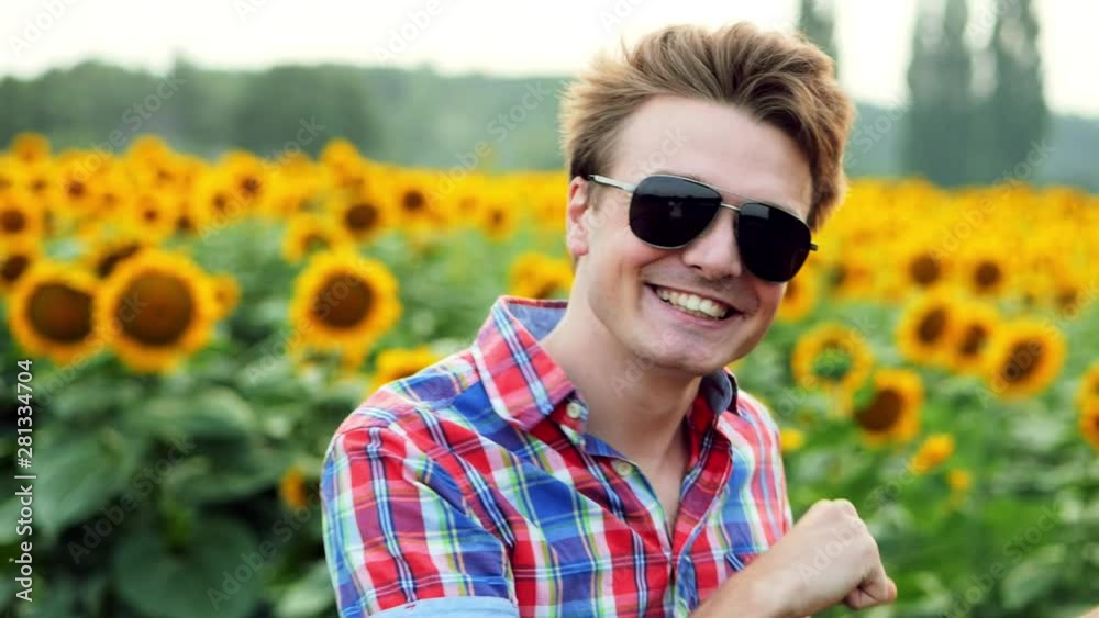 Portrait of cool male-farmer in sunglasses dancing fun on sunflowers