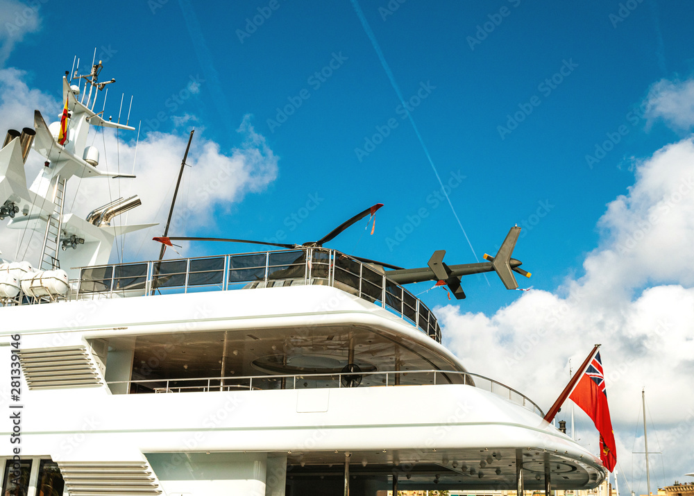 Naklejka premium Side view of new modern luxury yacht in Barcelona Yacht Port with modern and exclusive helicopter on the heliport rooftop flagpole wih Cayman Islands flag