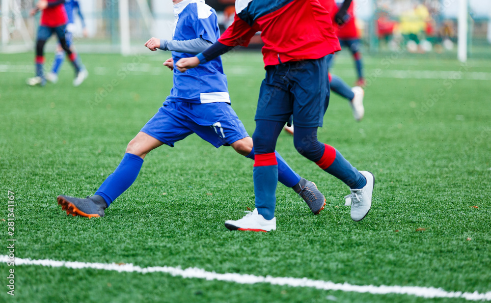 Boys in white and blue sportswear plays  football on field, dribbles ball. Young soccer players with ball on green grass. Training, football, active lifestyle for kids concept 