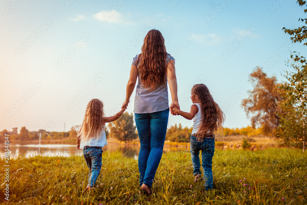 Family walking by summer river at sunset. Mother and her daughters having fun outdoors.