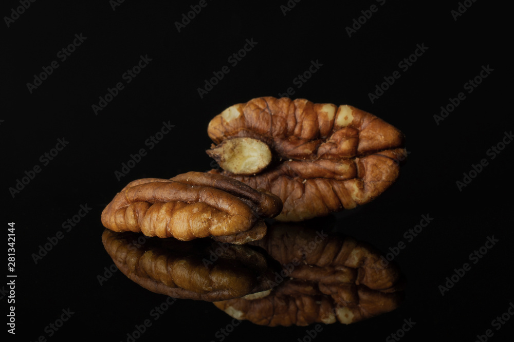 Group of two whole bright fresh brown pecan nut half isolated on black glass Group of two whole bright fresh brown pecan nut half isolated on black glass