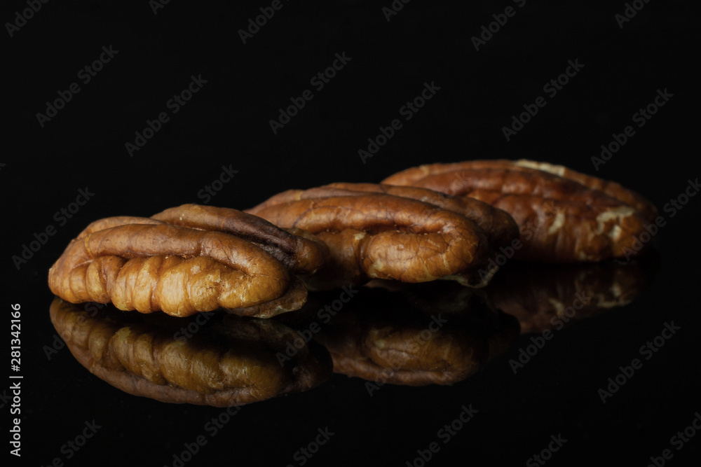 Group of three whole fresh brown pecan nut half in a row isolated on black glass