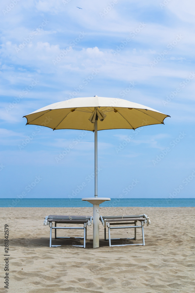 Pair of sun loungers and a beach umbrella on a deserted beach. Vacation and leisure concept