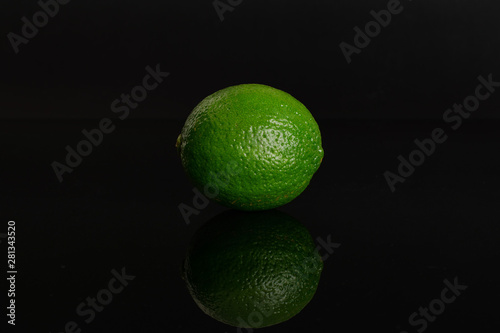 Fototapeta Naklejka Na Ścianę i Meble -  One whole fresh green lime isolated on black glass