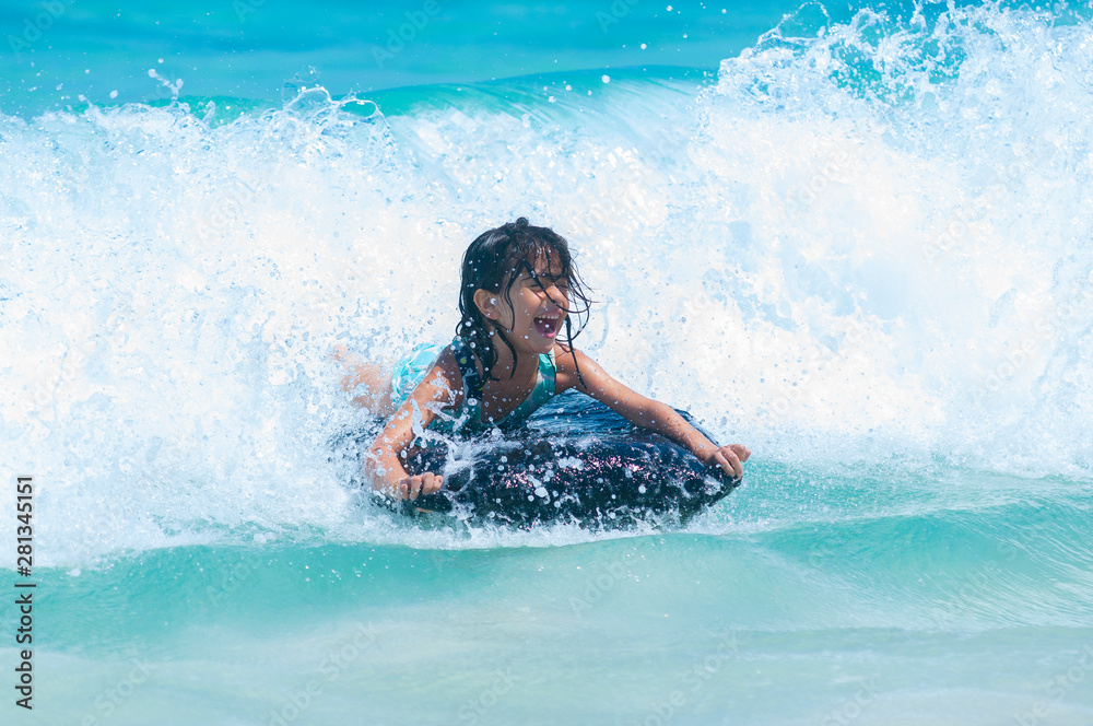 Young girl having crazy fun bodysurfing crashing waves while vacationing in beautiful tropical beach