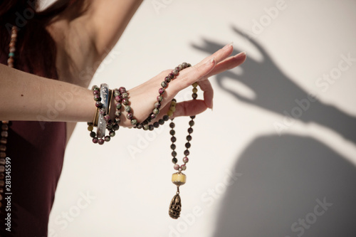 The elegant hand of a woman holding a mala yoga prayer bead necklace and shadow of hand on the background. 