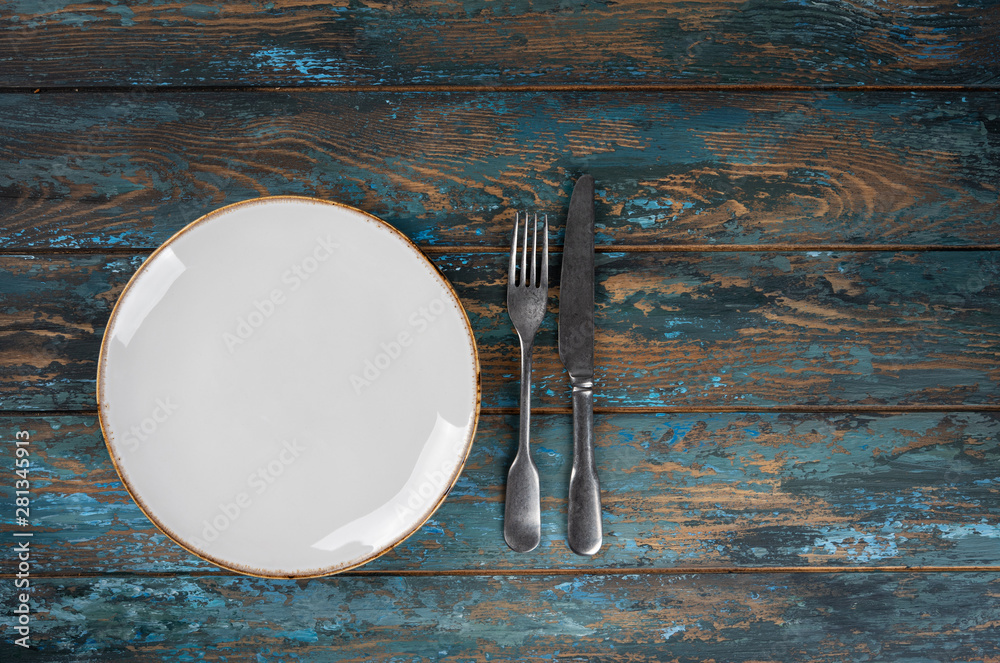 Empty plate with fork and knife on colored wooden background, top view, copy space, mock-up