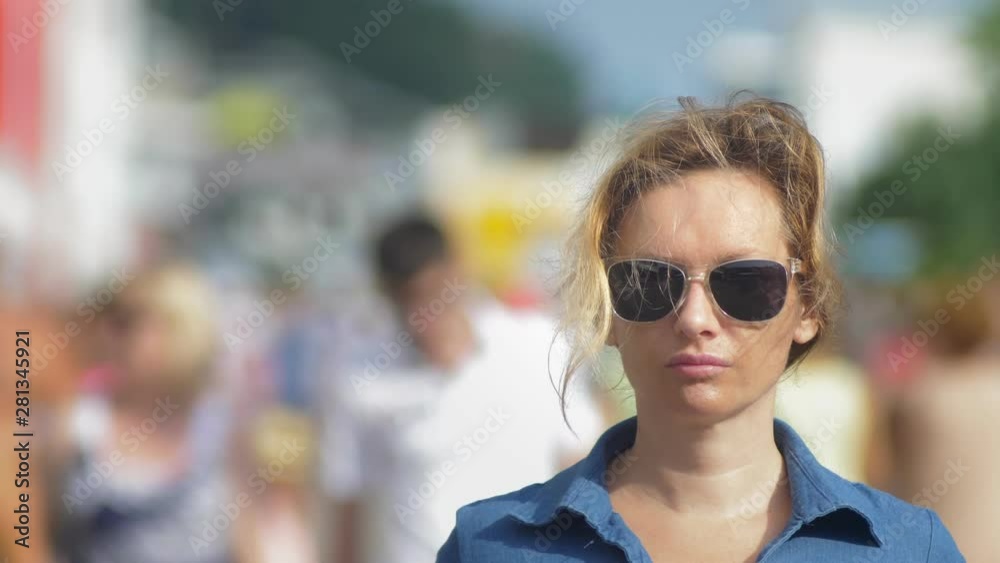 Beautiful woman in sunglasses, looking at camera, close-up. hot summer day. Moving crowd of people blurred in motion in the background. Beautiful woman in sunglasses, looking at camera, close-up. hot summer day. Moving crowd of people blurred in motion in the background.