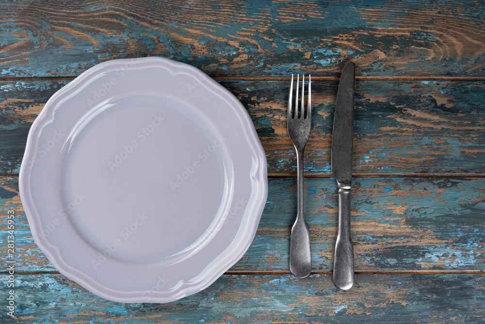 Empty plate with fork and knife on colored wooden background, top view, copy space, mock-up