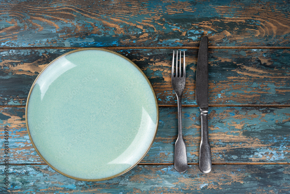 Empty plate with fork and knife on colored wooden background, top view, copy space, mock-up