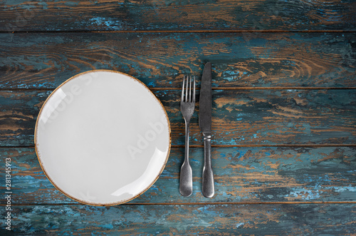 Obraz na płótnie Empty plate with fork and knife on colored wooden background, top view, copy space, mock-up w salonie
