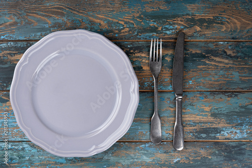 Empty plate with fork and knife on colored wooden background, top view, copy space, mock-up