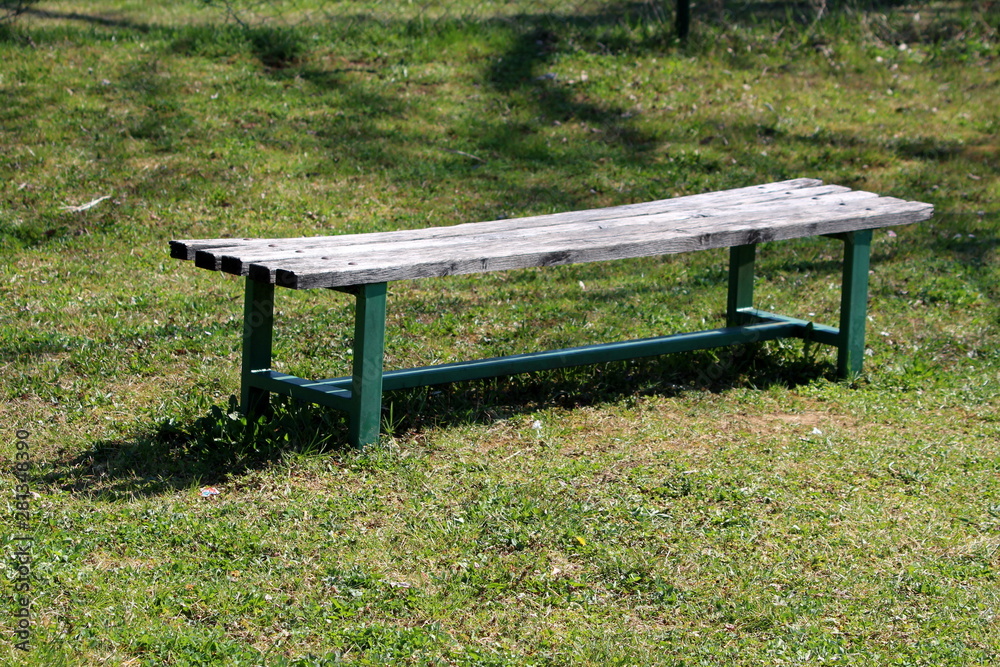 Old public park bench with wooden seat and green metal support frame surrounded with freshly cut grass in local park on warm sunny spring day Old public park bench with wooden seat and green metal support frame surrounded with freshly cut grass in local park on warm sunny spring day