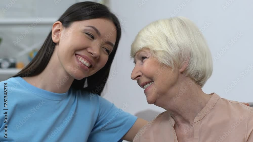 Friendly young lady smiling at happy senior lady, aid to seniors, family care Friendly young lady smiling at happy senior lady, aid to seniors, family care