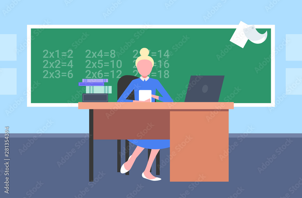 female teacher sitting at desk in front of chalkboard using laptop math lesson education concept modern school classroom interior horizontal flat female teacher sitting at desk in front of chalkboard using laptop math lesson education concept modern school classroom interior horizontal flat