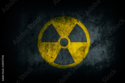 Radioactive (atomic nuclear ionizing radiation) danger warning yellow symbol shape painted on massive concrete cement wall grungy texture dark background. Nuclear radioactive alert concept.