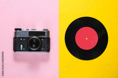 Retro still life, 70s. Vinyl record and film camera on pink yellow background. Top view. Flat lay