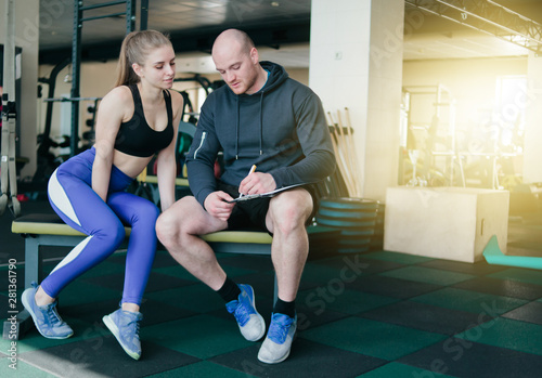 Fototapeta Naklejka Na Ścianę i Meble -  The concept of personal training. Instructor notes in notebook results  training sporty blonde woman sitting on a bench. Smiling sports couple