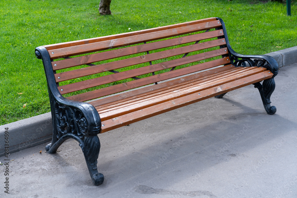 wooden bench with wrought iron flanks stands on sidewalk in city park wooden bench with wrought iron flanks stands on sidewalk in city park