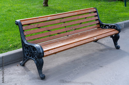 Fototapeta Naklejka Na Ścianę i Meble -  wooden bench with wrought iron flanks stands on sidewalk in city park