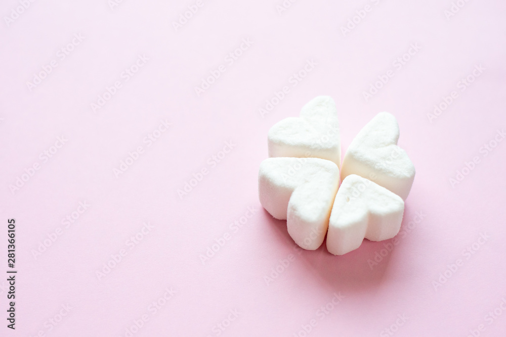 Four white hearts on a pink background. White heart-shaped marshmallows.