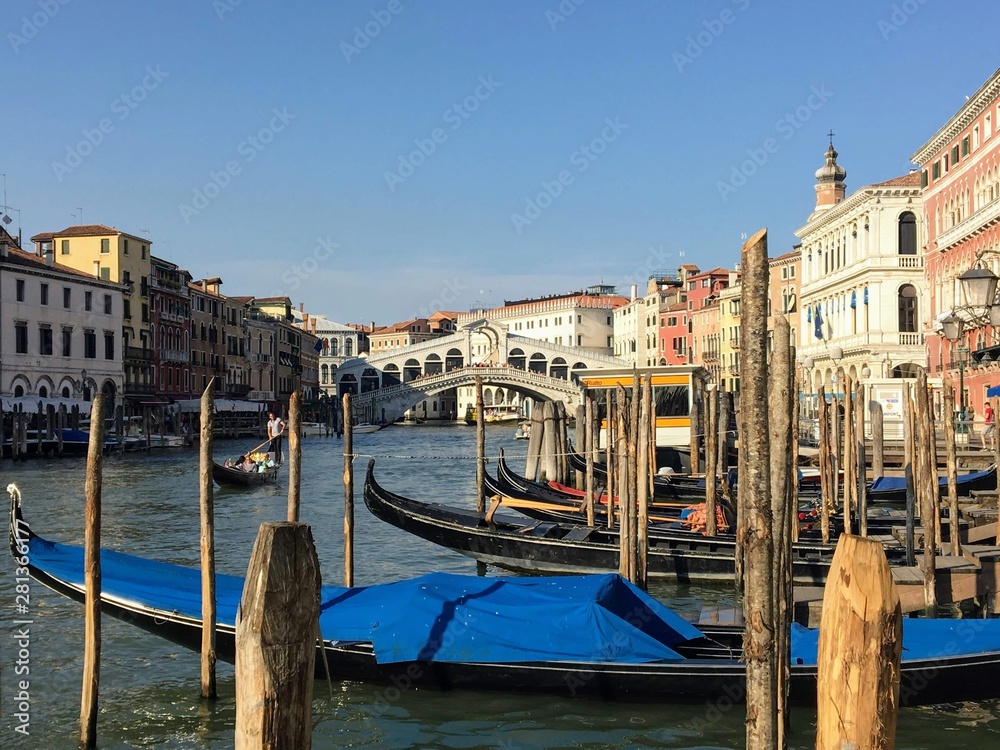 A classic view looking past wooden jetties and gondolas towards the Rialto Bridge in Venice, Italy along the Grand Canal on a beautiful summer day.