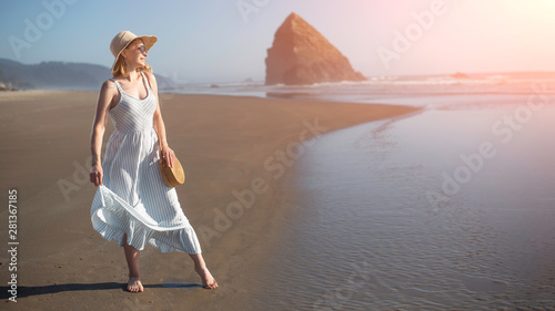 Girl in a hat with a wicker bag at sunset near the ocean with a rock. Women s style and fashion  relaxing on the beach  walking