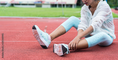 Young girl suffering or injury leg after exercise. Asian woman or student has pain in his foot or shin while running track has calf cramp and touching hurt leg or sprained ankle during workout