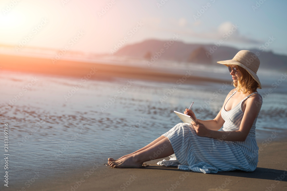 A young girl in sunglasses draws on a tablet on the ocean at sunset, freelancing, making money on the Internet, getting money on the Internet