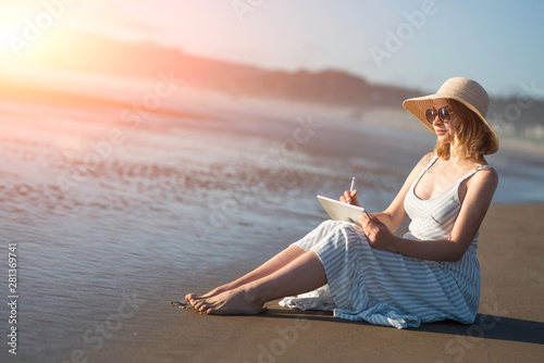 A young girl in sunglasses draws on a tablet on the ocean at sunset, freelancing, making money on the Internet, getting money on the Internet © Anton