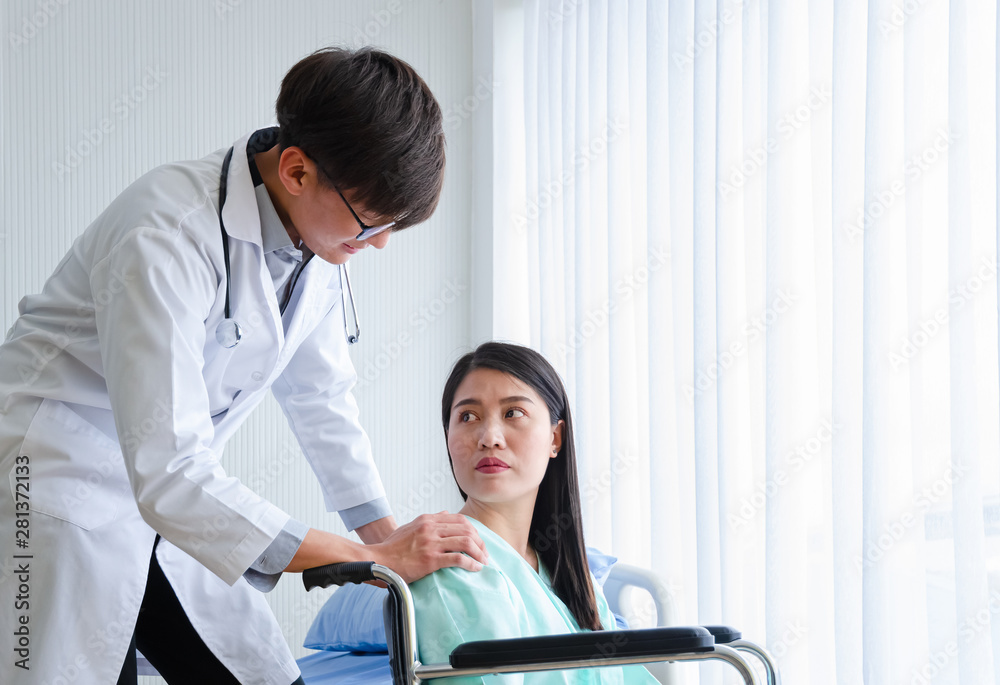 Obraz premium Asian male physician doctor encourage disabled female patient sitting on wheelchair in white hospital room