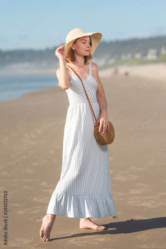 Girl in a hat with a wicker bag at sunset near the ocean with a rock. Women's style and fashion, relaxing on the beach, walking Girl in a hat with a wicker bag at sunset near the ocean with a rock. Women's style and fashion, relaxing on the beach, walking