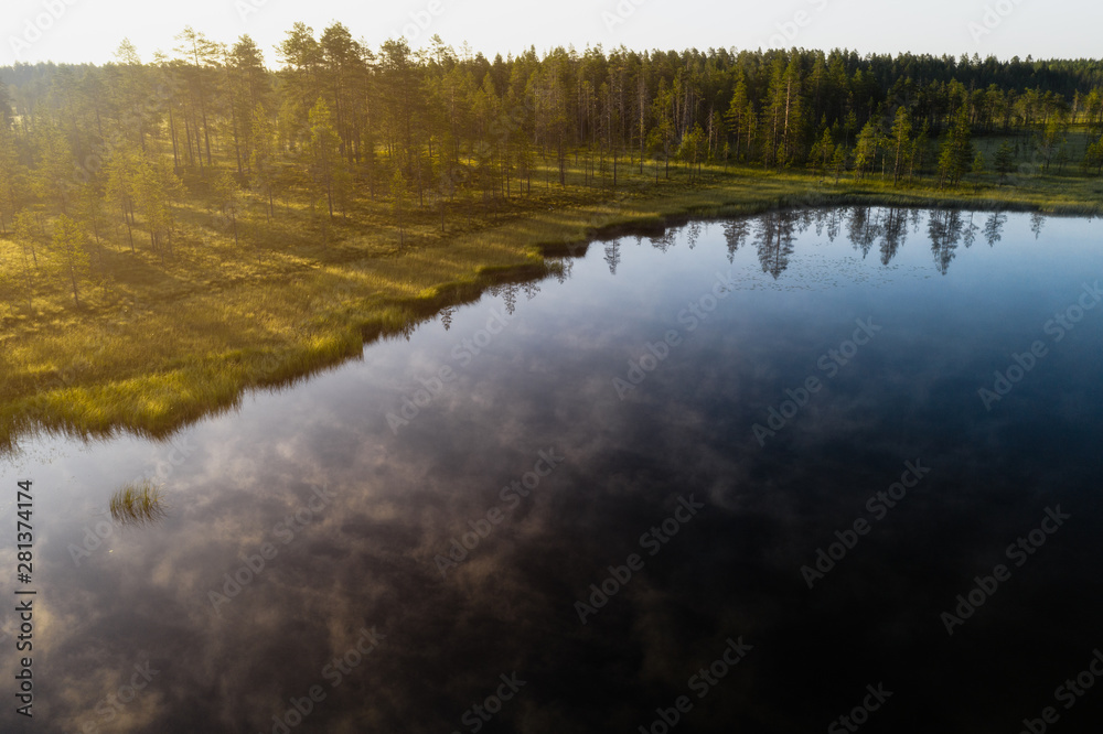 Aerial view of a calm and misty lake with forest in the background during golden sunrise