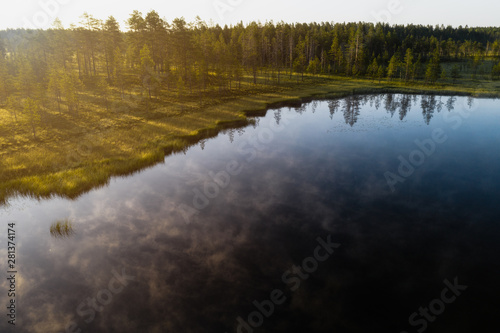 Aerial view of a calm and misty lake with forest in the background during golden sunrise