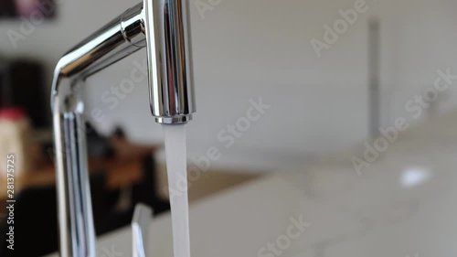 Closeup of chrome faucet in modern kitchen with caucasian woman hand opening and closing water