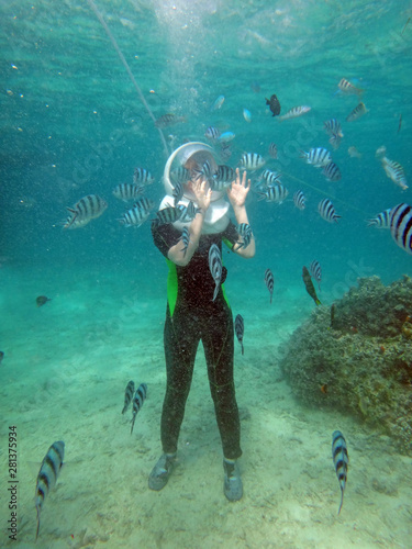 Tourist Walking underwater on seabed among school of fish
