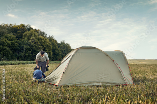 Family set up tent camp at sunset, beautiful summer landscape. Tourism, hiking and traveling in nature.