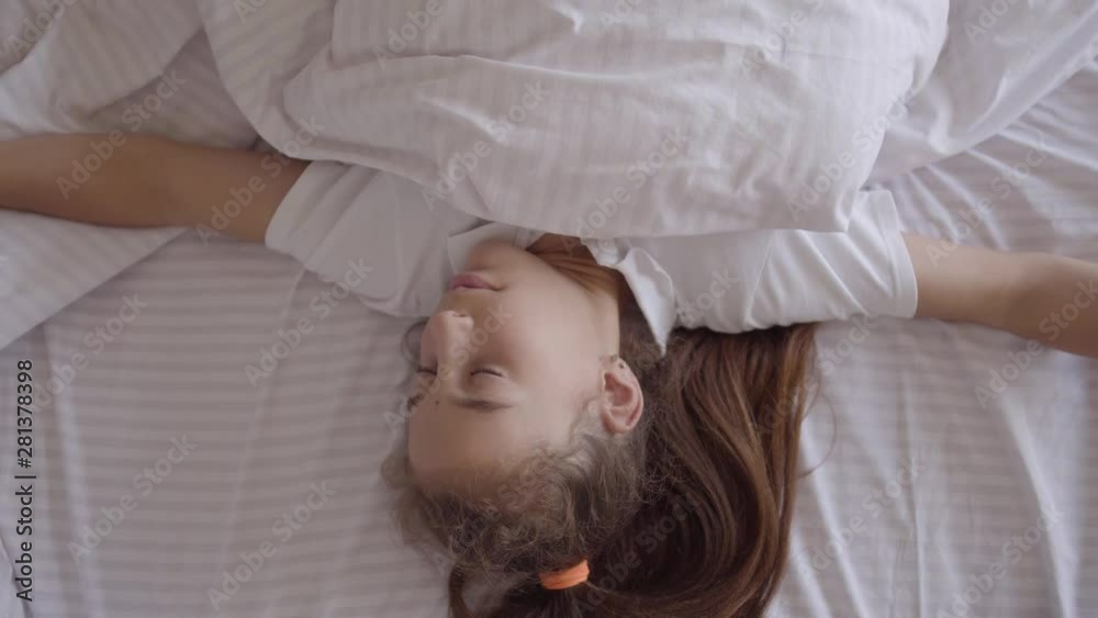 Adorable small girl sleeping in the bed at home. Girl waking up from an alarm clock on her smart watch. Modern technology. Carefree childhood. Adorable small girl sleeping in the bed at home. Girl waking up from an alarm clock on her smart watch. Modern technology. Carefree childhood.