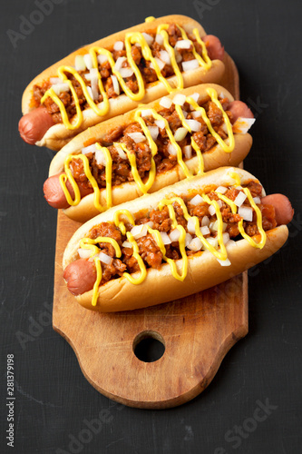 Homemade Detroit style chili dog on a rustic wooden board on a black background, low angle view. Close-up.