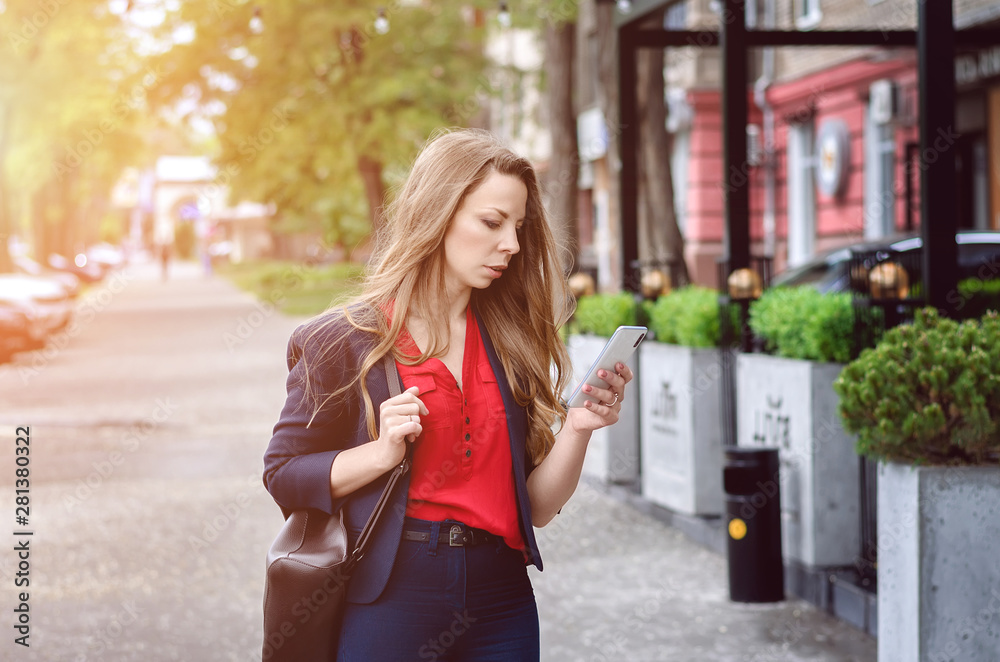 Beautiful young woman using smartphone near coffee shop cafe. Portrait of a girl reading or typing text message on mobile phone outdoors