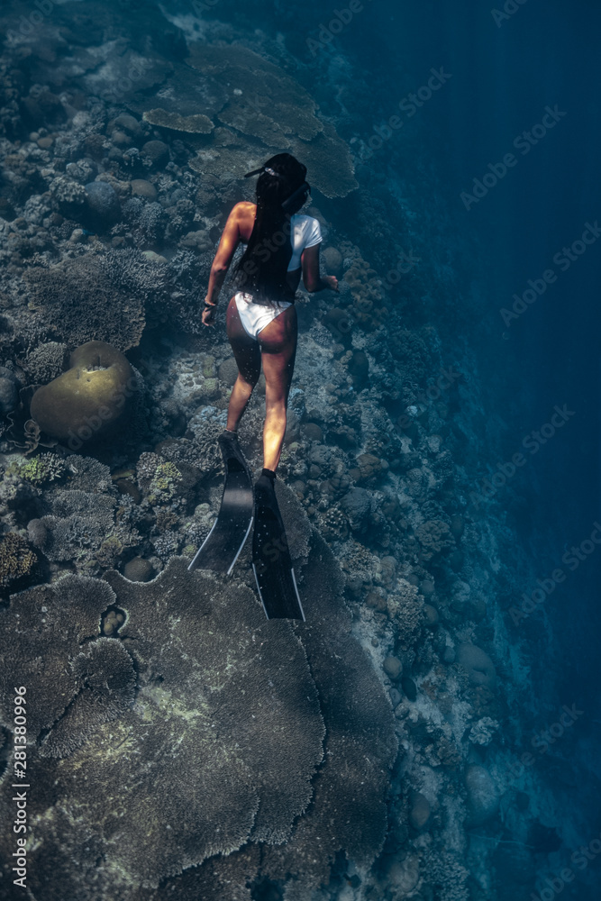 Young woman in a sexy swimwear ascends to the surface after a deep dive.