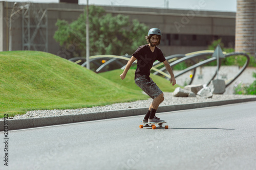 Skateboarder doing a trick at the city's street in sunny day. Young man in equipment riding and longboarding on the asphalt in action. Concept of leisure activity, sport, extreme, hobby and motion.