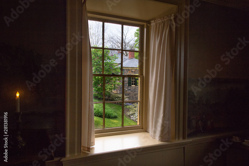 View of landscape with brick house through the old window. Mystic indow with curtains and candle