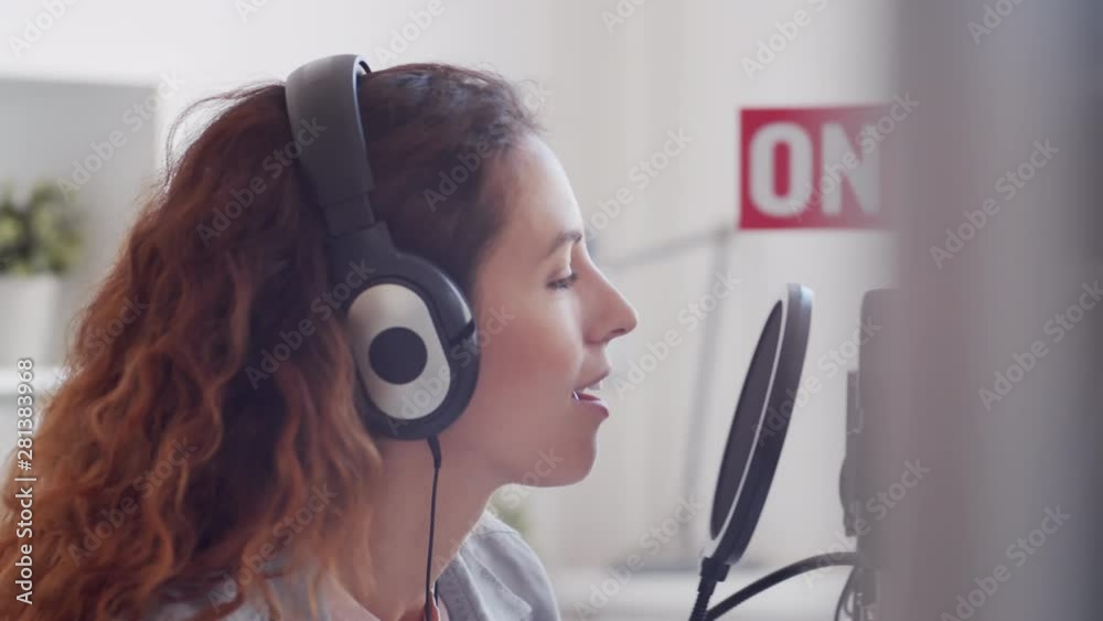 Close up of young Caucasian woman with curly hair putting on headphones and starting broadcasting in broadcast studio Close up of young Caucasian woman with curly hair putting on headphones and starting broadcasting in broadcast studio