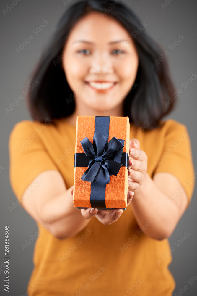 Portrait of Asian woman holding present with ribbon giving to you and smiling isolated on grey background focus on foreground Portrait of Asian woman holding present with ribbon giving to you and smiling isolated on grey background focus on foreground