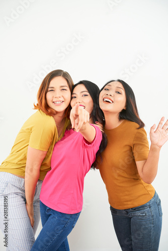 Portrait of three happy friends embracing each other and posing at camera over white background