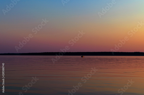 Sunset in the sea with a small fishing boat at the lake. A picture of a small fishingboat with a beautiful sunset background. Water surface with reflections