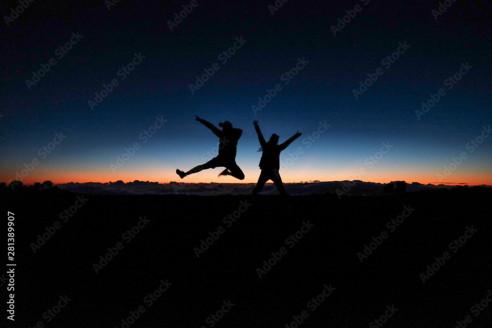 silhouette of two people jumping in front of a sunset skyline