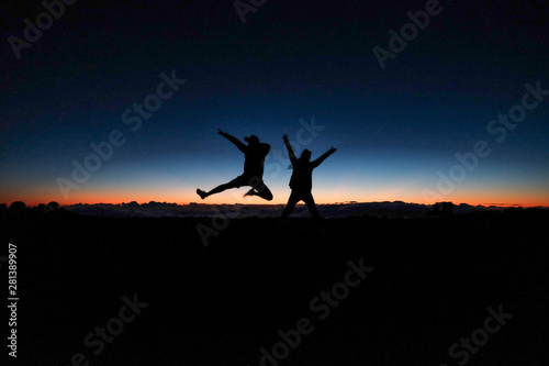 silhouette of two people jumping in front of a sunset skyline