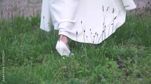 Bride's feet walking away on white high heels in green grass, slow motion photo